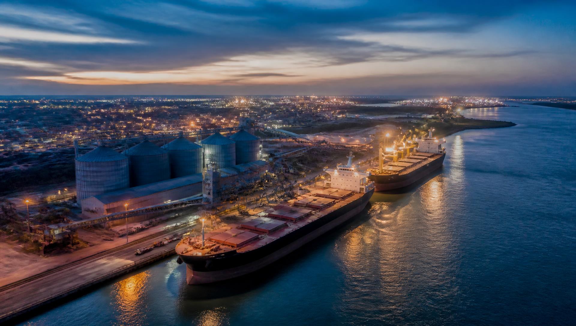 Bulk export terminal at dusk with silos and berthed vessels